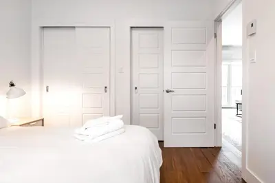 a white bedroom with white doors and wooden floors at Hip, Stylish Apartment In Little Italy by Den Stays in Montréal