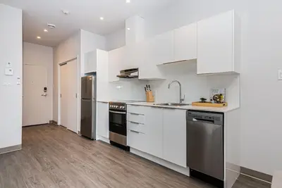 a kitchen with white cabinets and stainless steel appliances at Brand New and Perfectly Located Flat in Le Plateau by Den Stays in Montréal
