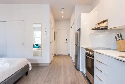 a kitchen with white cabinets and a bed in a room at Brand New and Perfectly Located Flat in Le Plateau by Den Stays in Montréal