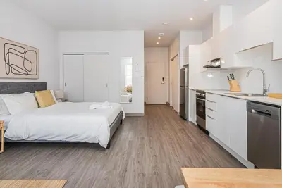 a white bedroom with a bed and a kitchen at Brand New and Perfectly Located Flat in Le Plateau by Den Stays in Montréal