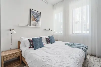 a white bedroom with a large bed with blue pillows at Bakan - Sainte Catherine in Montréal