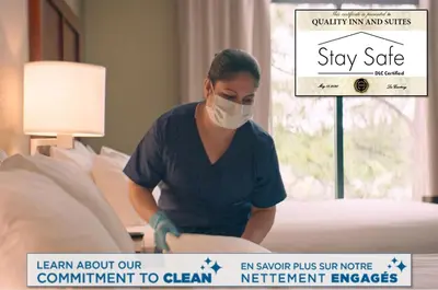 a woman in a mask is making a bed at Quality Inn & Suites PE Trudeau Airport in Dorval