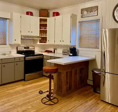 a kitchen with white cabinets and a stool in it at Bel appartement A la croisée des sommets in Notre-Dame-Des-Bois