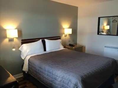 a hotel room with a bed with two lamps and a mirror at Olux Hotel-Motel-Suites in Laval