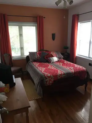 a bedroom with a bed with a red comforter and two windows at Magnolia B&B in Granby
