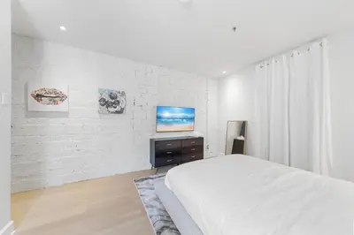 a white bedroom with a bed and a tv at Suites De la Montagne in Montréal