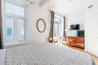 a white bedroom with a bed and a mirror at hotel le coach in Montréal