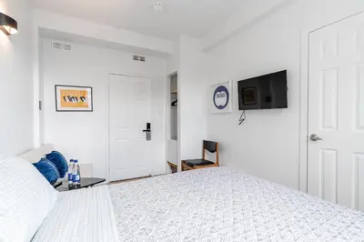 a white bedroom with a bed and a tv at hotel le coach in Montréal