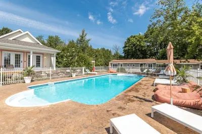 a swimming pool with chairs and an umbrella in front of a house at Hôtel le Rosay in Venise-en-Québec
