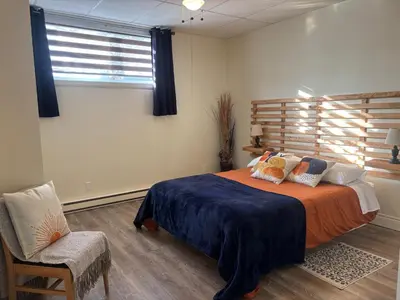 a bedroom with a bed and a chair and a window at Spacieux 4,5 Parfait pour des Vacances Confortables ! in Lac-Mégantic