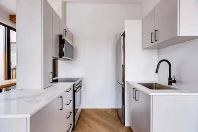 a white kitchen with a sink and a refrigerator at Le Virtuose - Vieux-Terrebonne in Terrebonne