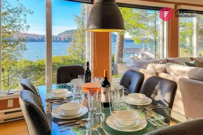 a dining room with a table and a view of the water at Aux Berges du Pont Suspendu / Grand Lac Brompton in Saint Denis de Brompton