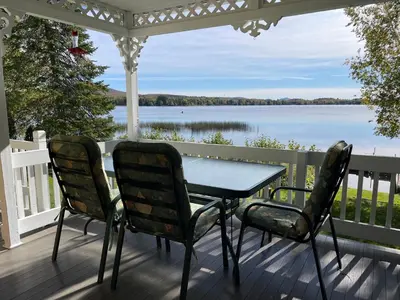 a table and chairs on a porch with a view of a lake at Chalet KLS Lac D'Argent in Eastman
