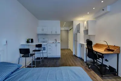 a bedroom with a bed and a desk and a kitchen at Laval stays 31 days minimum in Laval