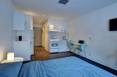 a bedroom with a bed and a kitchen with white cabinets at Laval stays 31 days minimum in Laval