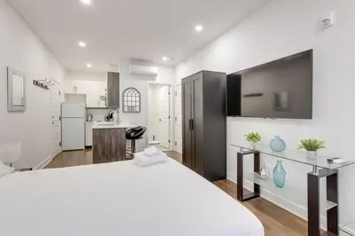 a white bedroom with a large bed and a kitchen at Le Mile End by M11 - Modern & Comfy Studio in Montréal