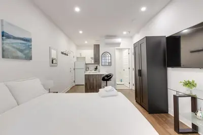 a white bedroom with a large bed and a kitchen at Le Mile End by M11 - Modern & Comfy Studio in Montréal