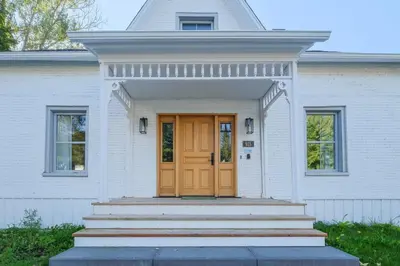 a white house with a brown door and stairs at Maison ancestrale complètement rénovée 4 chambres in Bromont