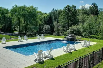 a swimming pool with chairs and a fountain at Maison 3 chambres à coucher vue sur la montagne in Bromont