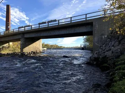 a bridge over a river with water rushing under it at La cachette de la rivière au saumon et spa in Scotstown
