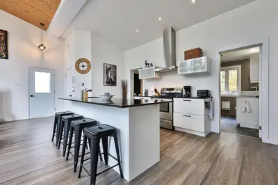 a kitchen with white cabinets and black counter stools at Chalet Le Cerf du Lac in Disraeli