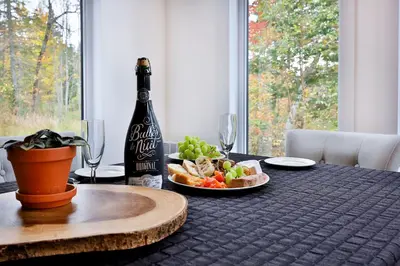 a bottle of wine and a plate of food on a table at Chalet Le Cerf du Lac in Disraeli