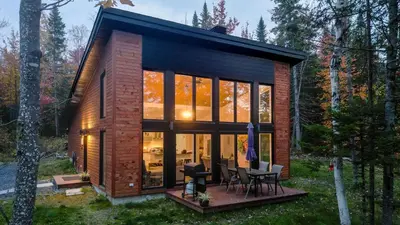 a tiny house in the woods with a lot of windows at Chalet Le Cerf du Lac in Disraeli