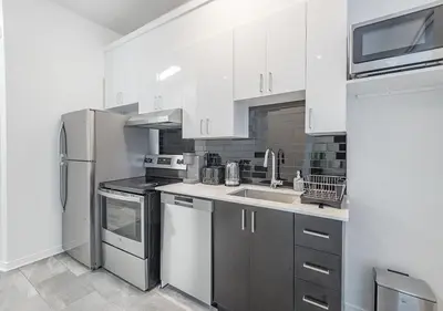 a kitchen with white cabinets and a stainless steel refrigerator at Luxurious 3BD Apt in heart of downtown 5 min walk to Bell Center in Montréal
