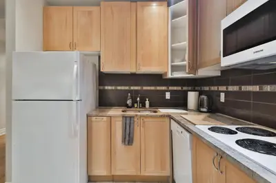 a kitchen with wooden cabinets and a white refrigerator at STUNNING full APARTMENTS - stocked KITCHENS - WASHER & DRYERS - WORKSPACE PROVIDED - FAST WIFI - LOCATED on the FAMOUS ST Denis street - Near METRO MONT ROYAL in Montréal