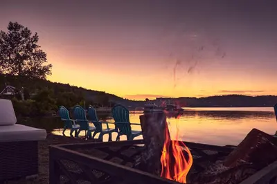 a group of chairs sitting around a campfire near a lake at Étoile du Lac Lyster - Spa & Vue sur le Lac in Coaticook